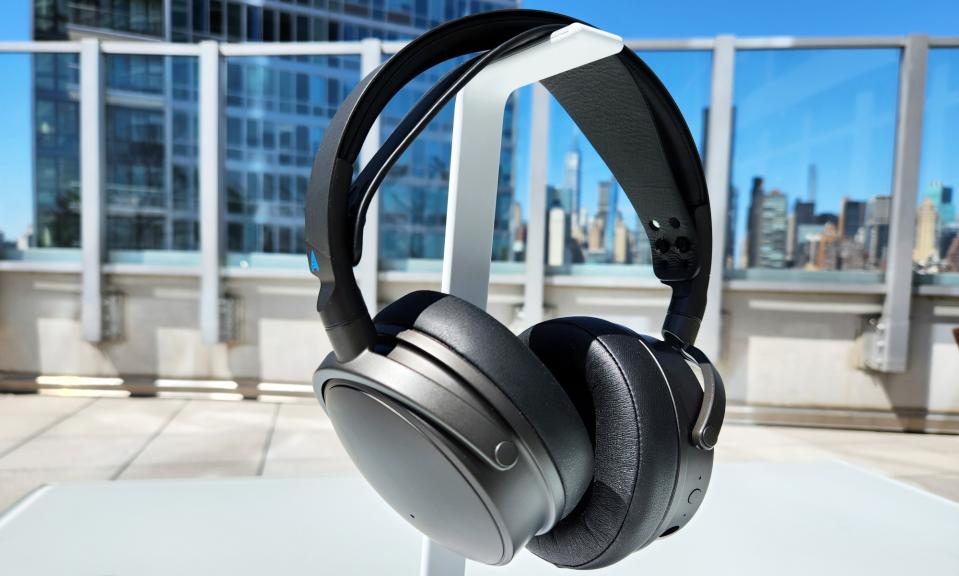 A black gaming headset, the Audeze Maxwell, rests on a white headphone stand on a table outdoors.